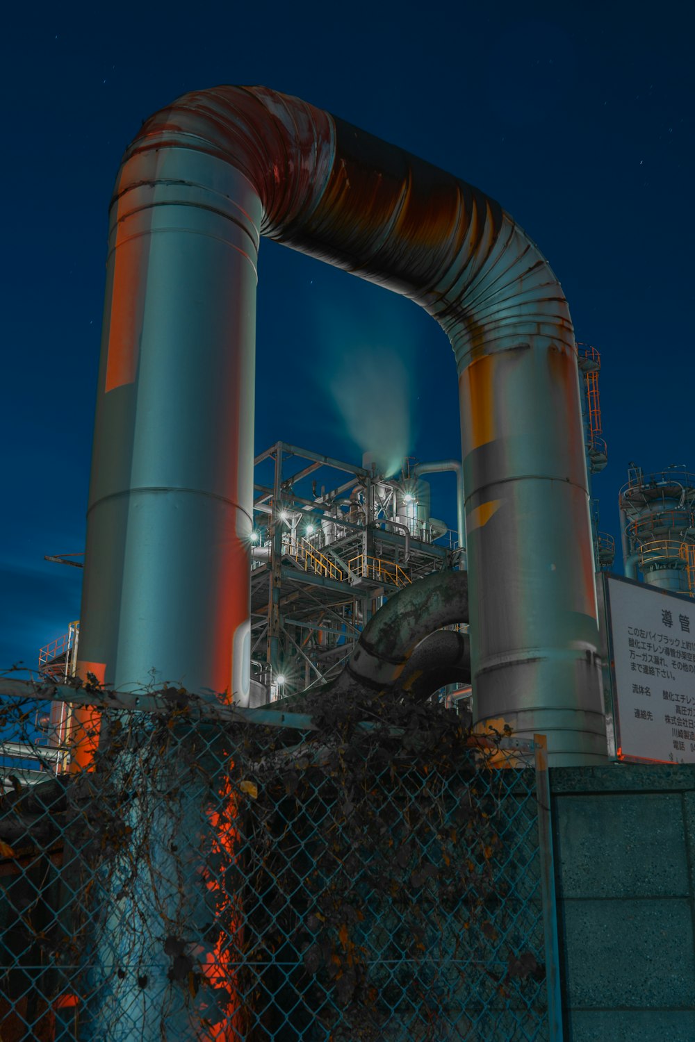 a large metal pipe near a fence with a building in the background