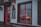 A storefront with red accents featuring a door and window. A chalkboard sign is displayed beside the door with writing in another language. Through the window, an illuminated decoration resembling a deer is visible. The scene is dimly lit, suggesting overcast weather.