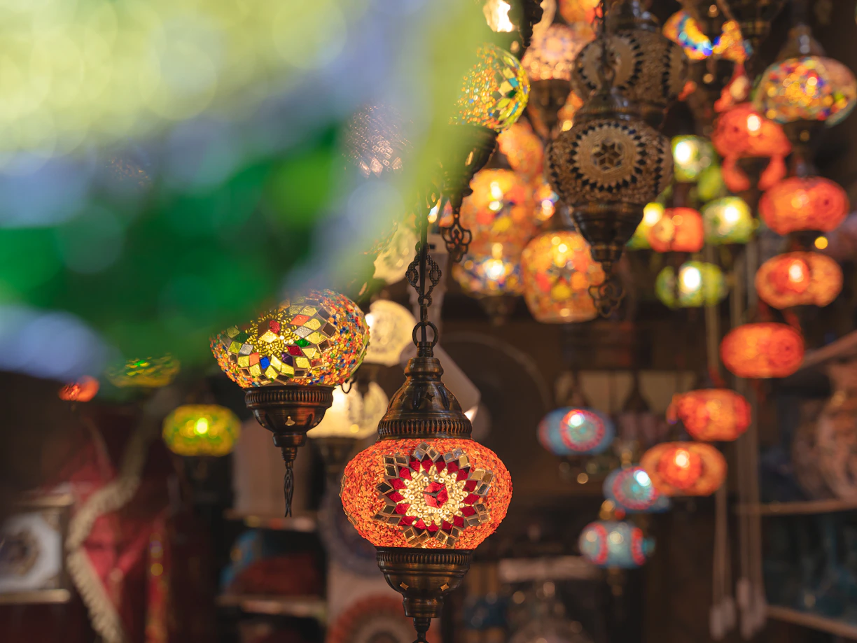 A vibrant Moroccan souk scene with colorful rugs, pottery, and lanterns displayed under warm sunlight.