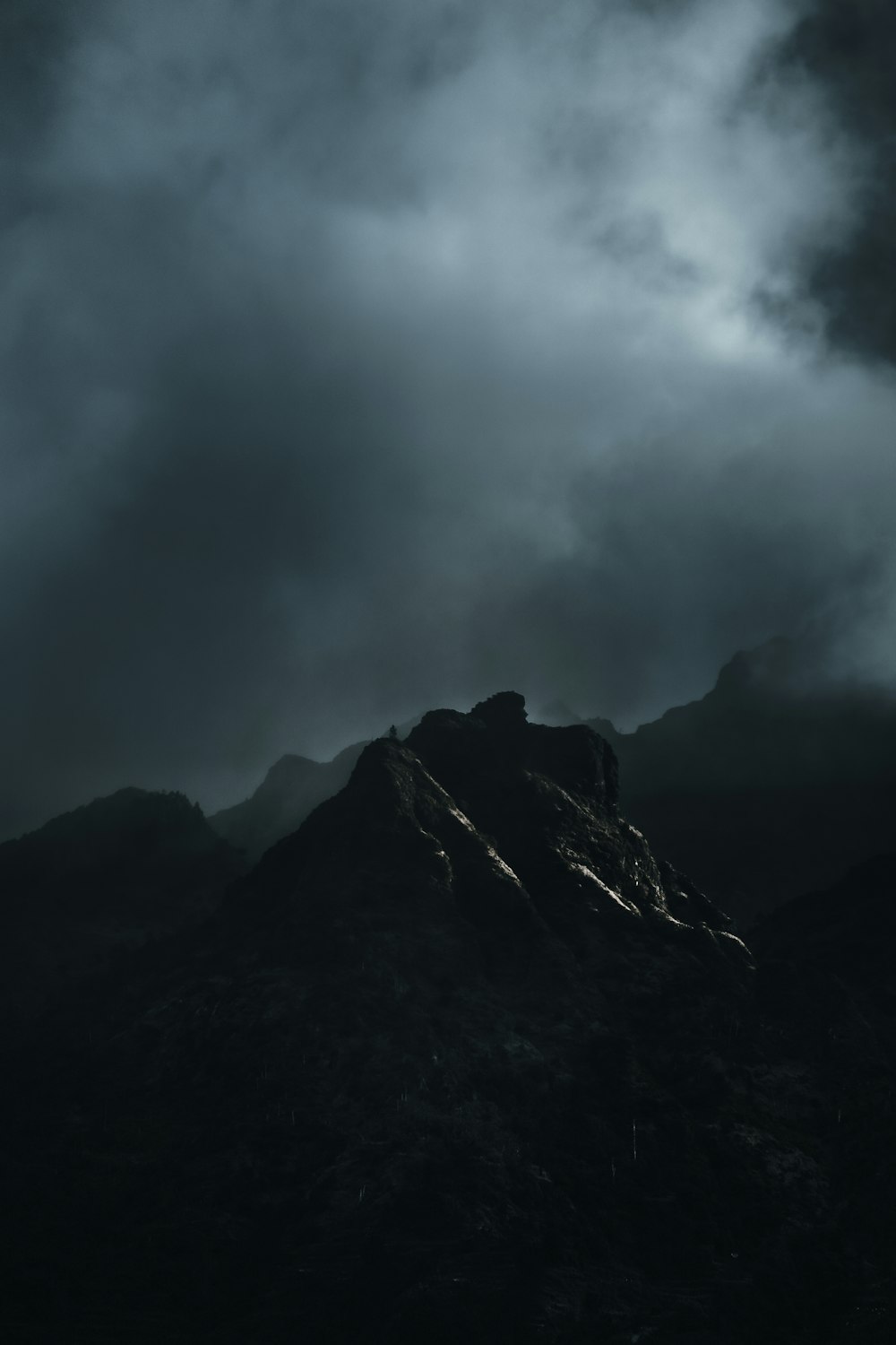 a black and white photo of a mountain under a cloudy sky