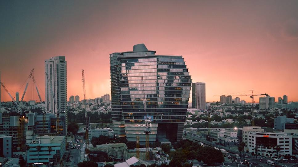 A modern residential building under construction with cranes in the background during sunset.
