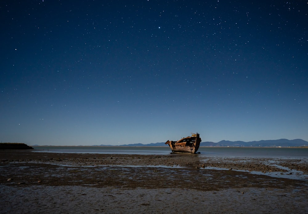 a boat sitting on top of a sandy beach under a night sky