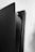 A close-up view of a sleek, modern gaming console standing vertically against a light wooden wall. The console has a two-tone color scheme, primarily black and white, with the brand name 'SONY' visible on the top right side.
