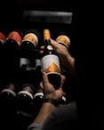 a person holding a bottle of wine in front of a rack of bottles