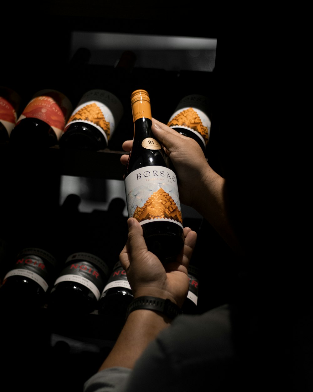 a person holding a bottle of wine in front of a rack of bottles