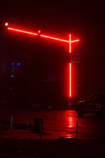 A vibrant urban street corner at dusk with glowing orange and red neon lights reflecting on wet pavement.