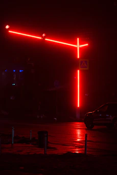 A vibrant urban street corner at dusk with glowing orange and red neon lights reflecting on wet pavement.