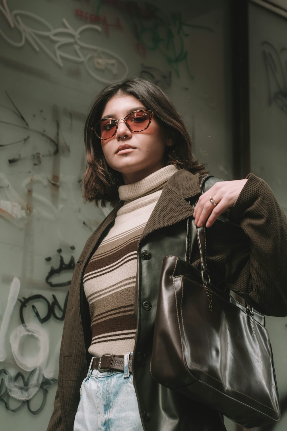 a woman holding a brown purse standing in front of a graffiti covered wall