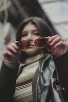 A stylish woman trying on oversized tortoiseshell sunglasses beside a bright window.