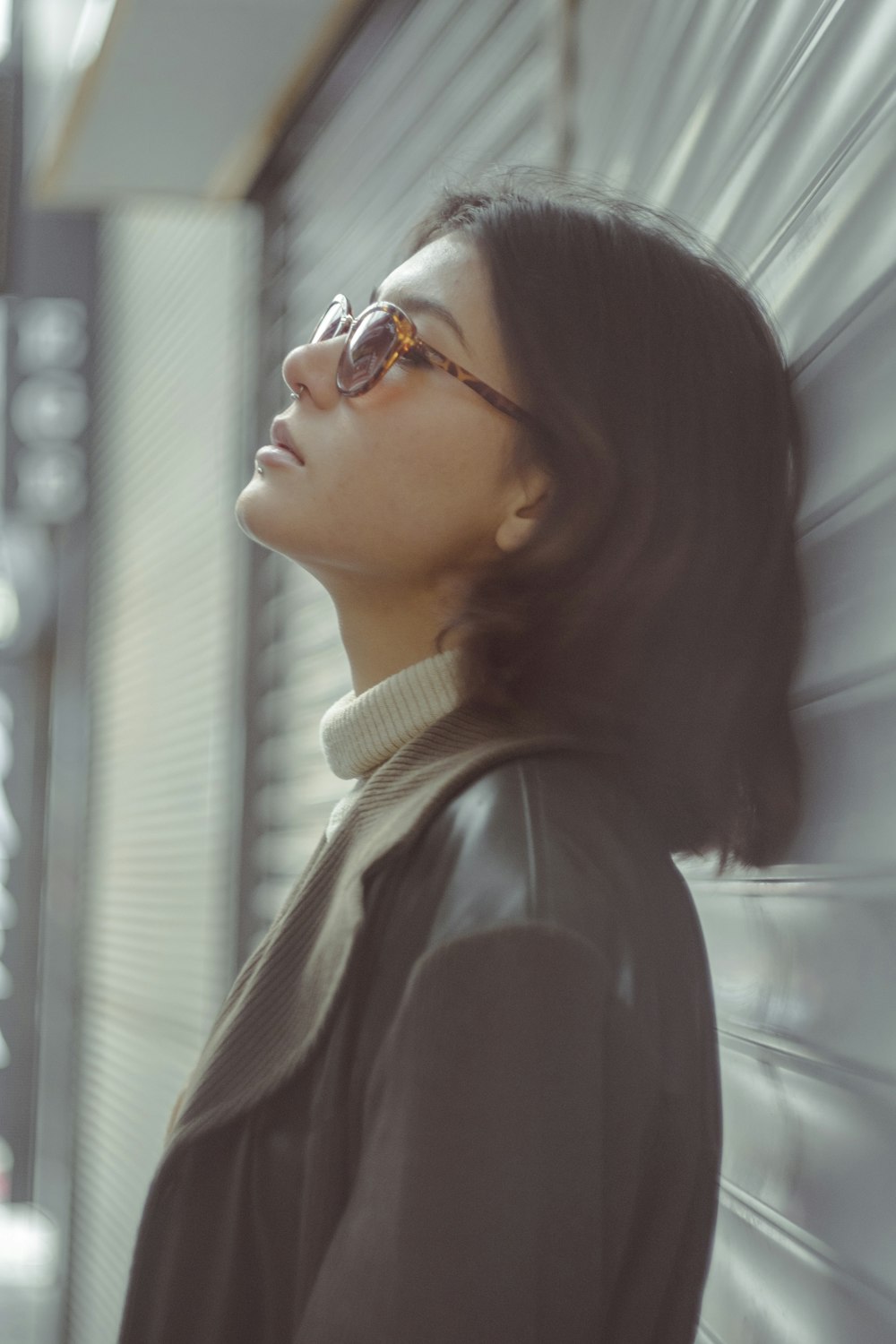 a woman wearing glasses leaning against a wall