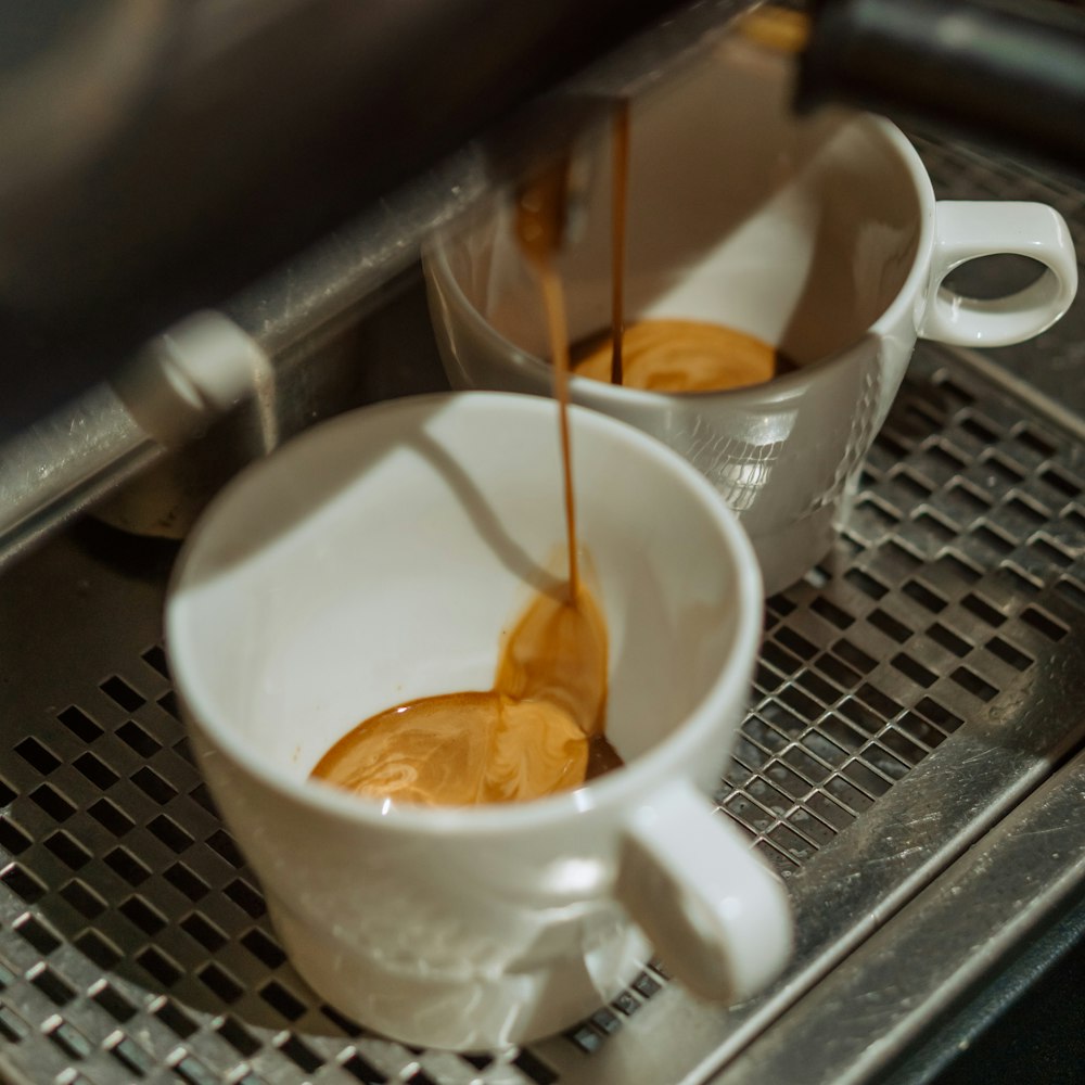 two cups of coffee being filled with liquid