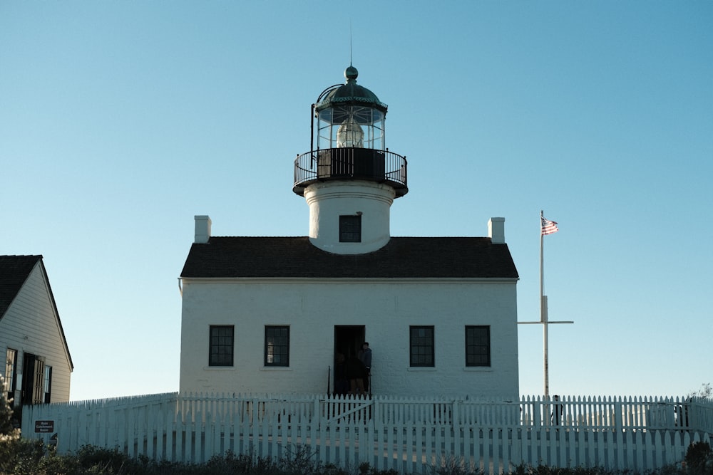 a white lighthouse with a black roof and a white picket fence