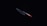 A sharp kitchen knife with a metallic blade and a red handle is illuminated against a dark background, emphasizing its sleek and shiny appearance.