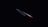 A sharp kitchen knife with a metallic blade and a red handle is illuminated against a dark background, emphasizing its sleek and shiny appearance.