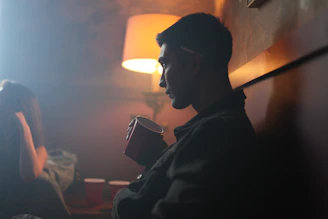Illustration of a grumpy older man holding a coffee cup in a dimly lit recovery meeting room with folding chairs.