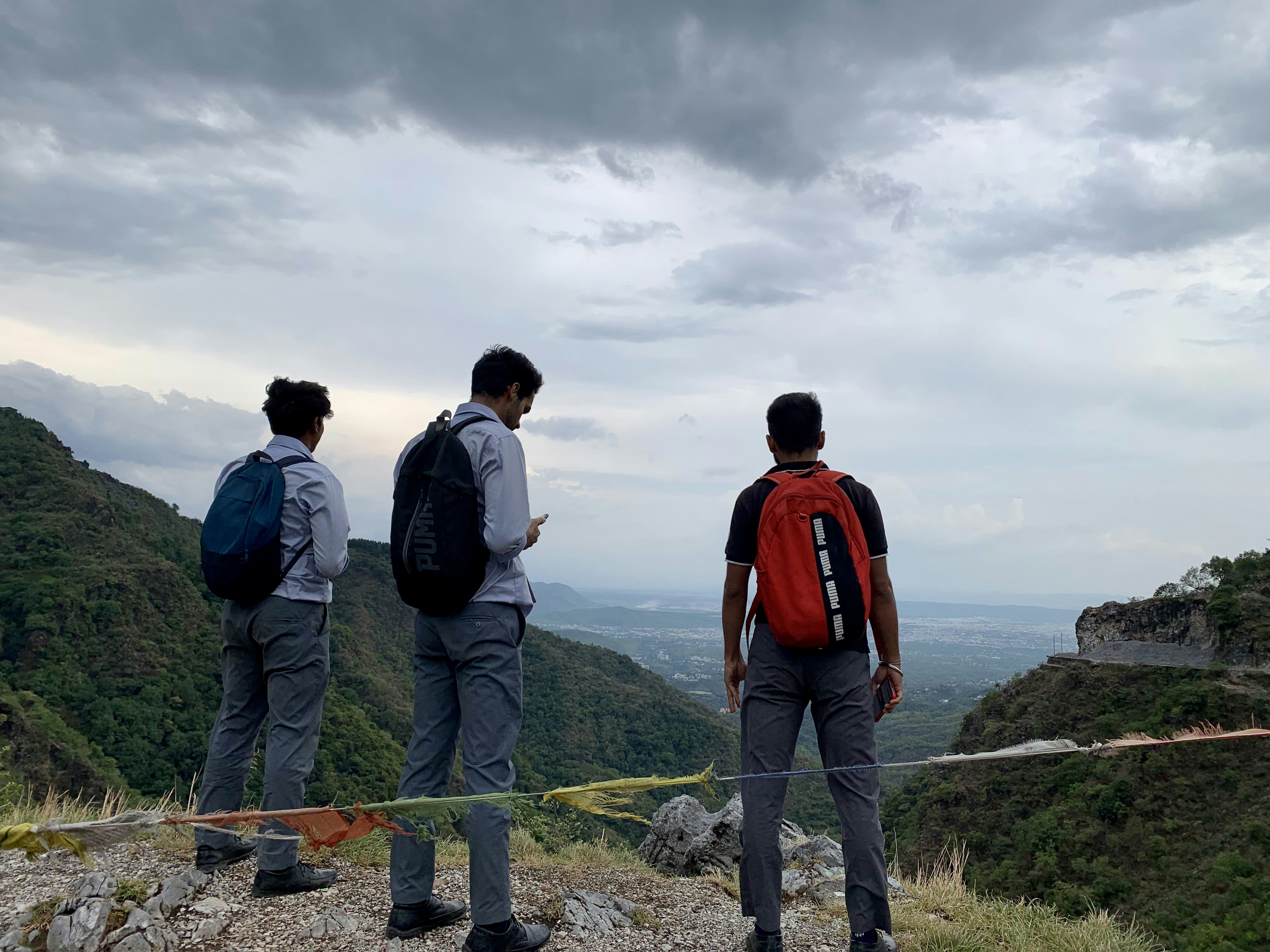 Group of friends on mountain trek with backpacks, scenic valley below, laughing and enjoying adventure