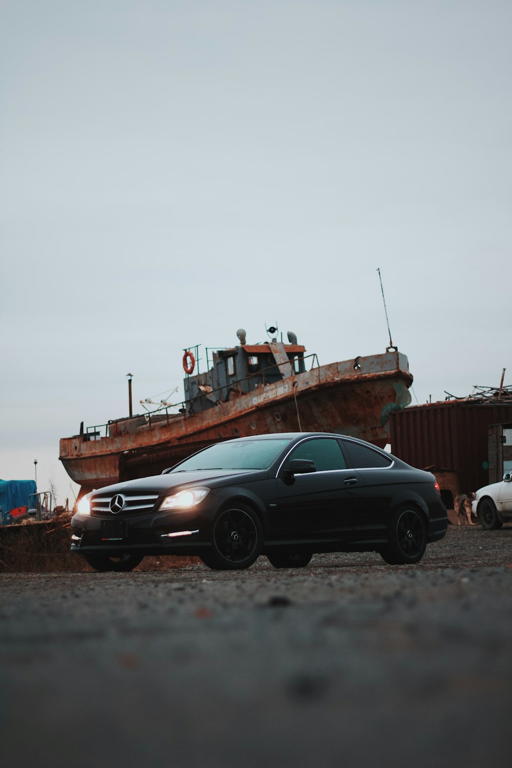 a black car parked in front of a rusted boat