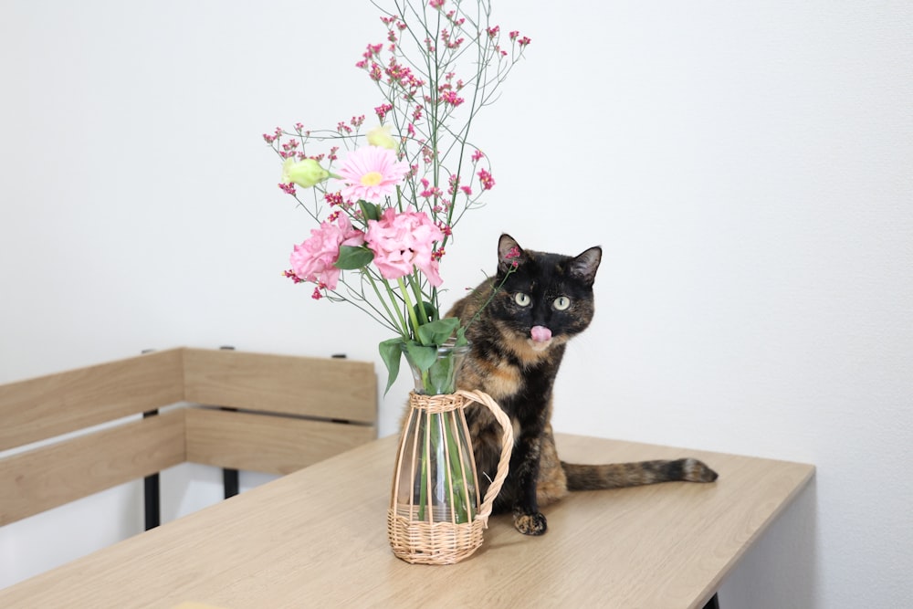 um gato sentado em uma mesa ao lado de um vaso de flores