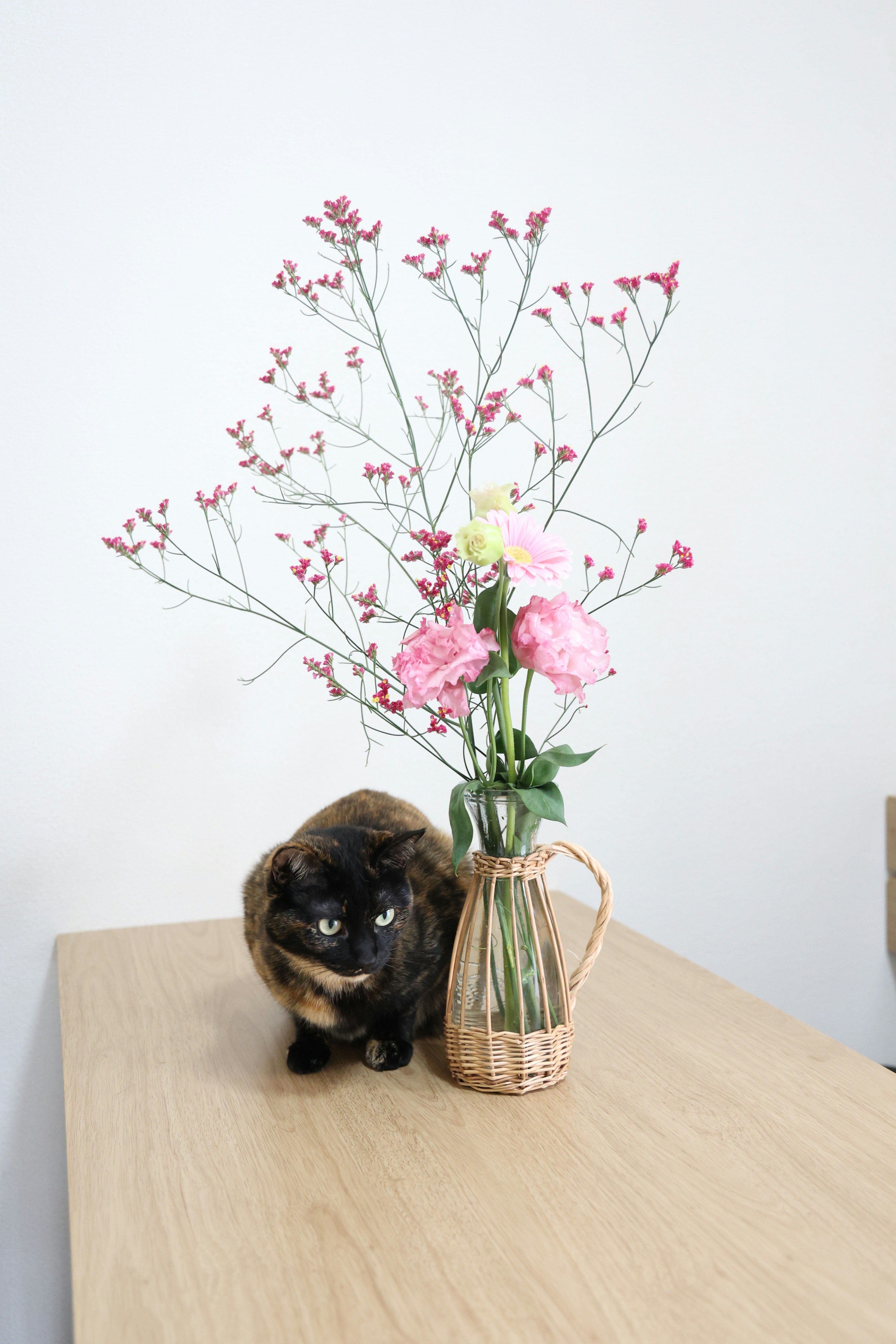 a cat sitting on a table next to a vase with flowers