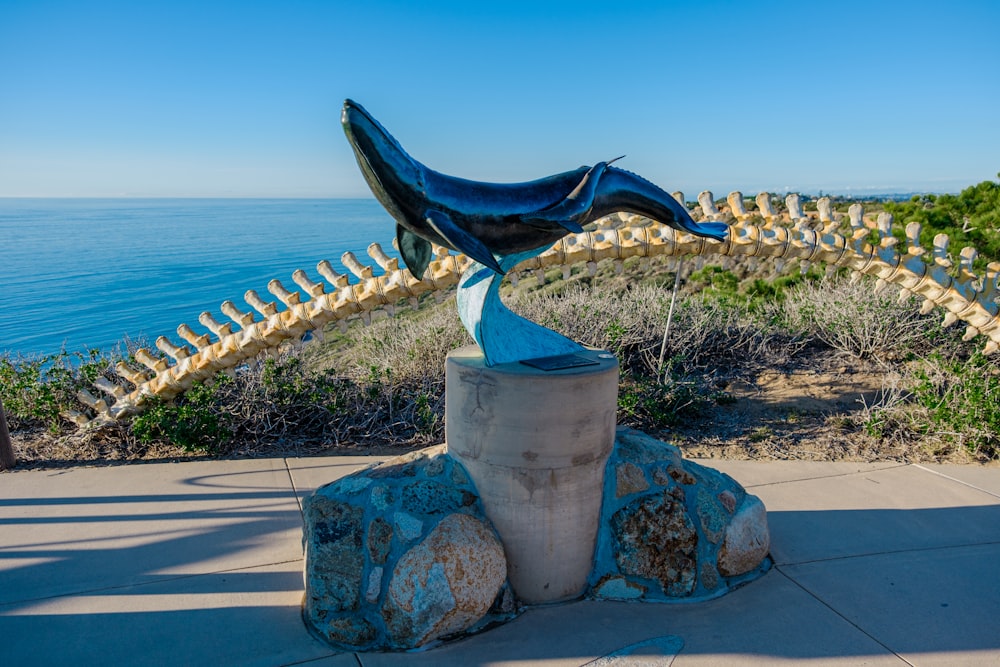 a sculpture of a dolphin on a rock near the ocean