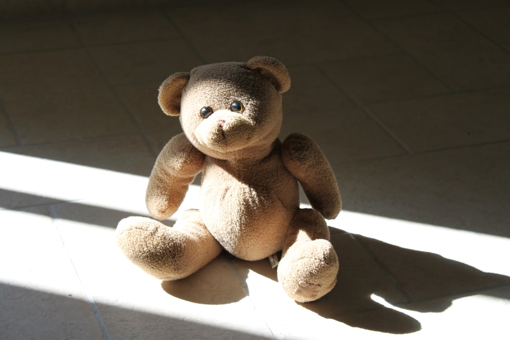 a brown teddy bear sitting on a tile floor
