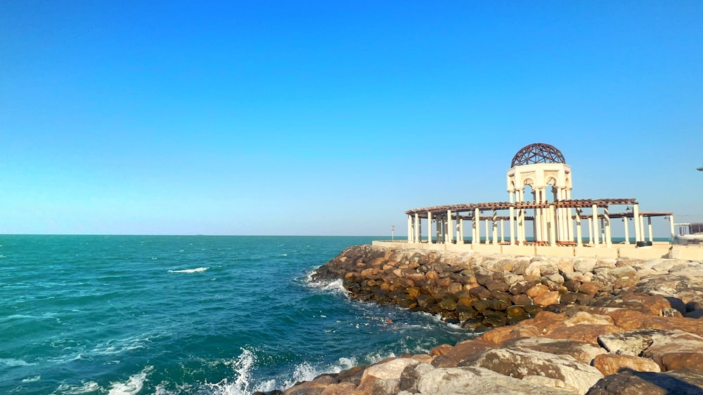 a gazebo sitting on top of a rocky shore next to the ocean