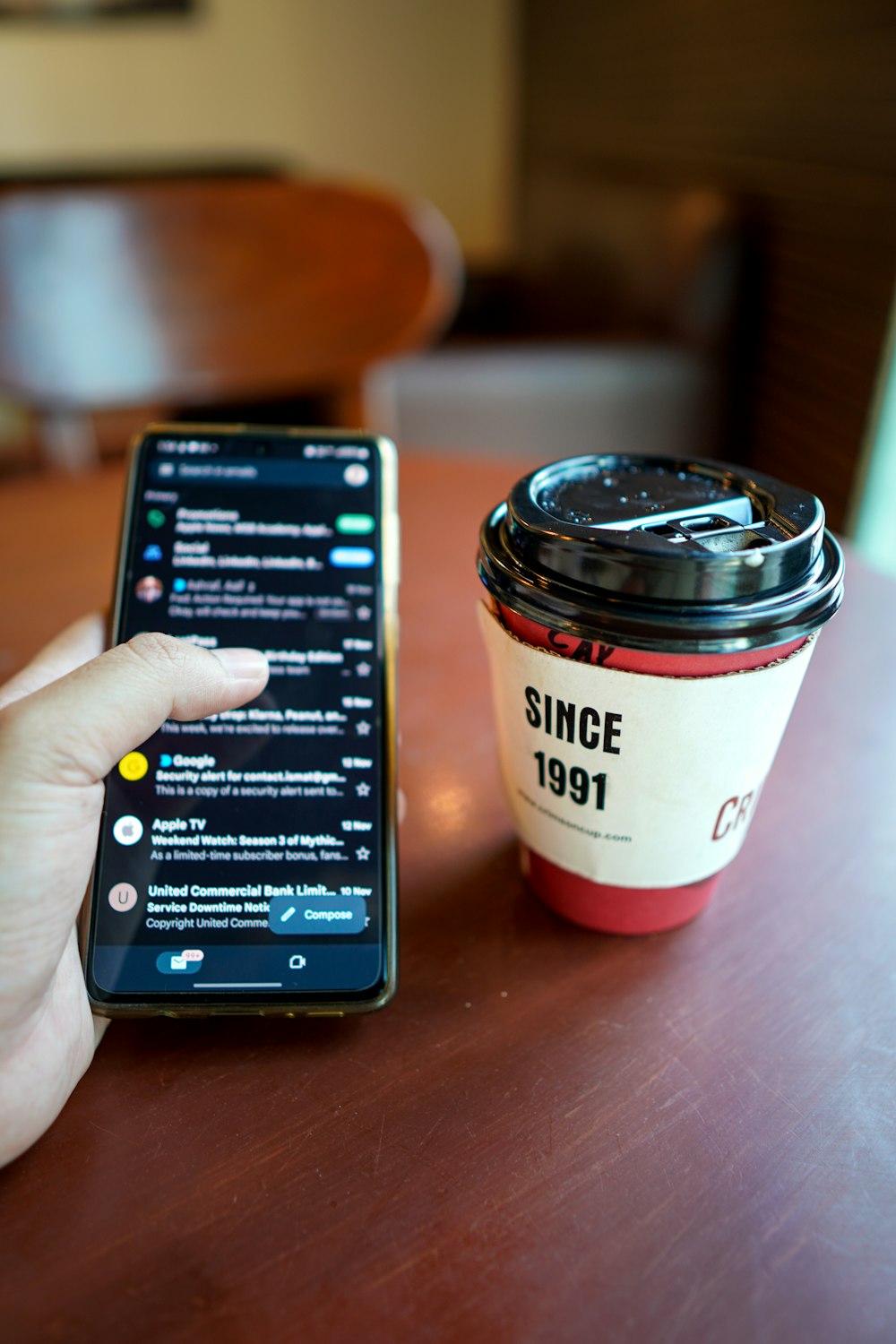 a person holding a cell phone next to a cup of coffee