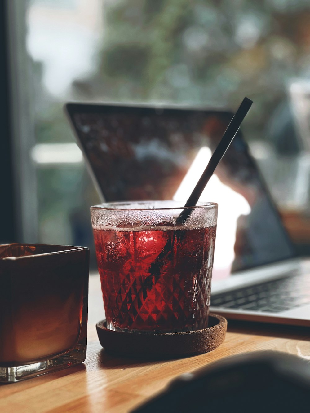 a glass of liquid sitting on a table next to a laptop