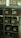 A set of metal shelves filled with cardboard boxes, each labeled with handwritten notes. The shelves are located in a storage area, possibly a warehouse or archive, with additional boxes in the background. The lighting is dim, creating a somewhat shadowy environment.