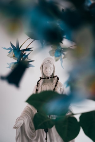 A serene statue of the Virgin Mary surrounded by flowers.