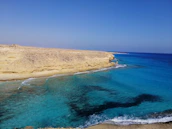 A coastal view of rugged cliffs meeting turquoise waters under a clear blue sky.