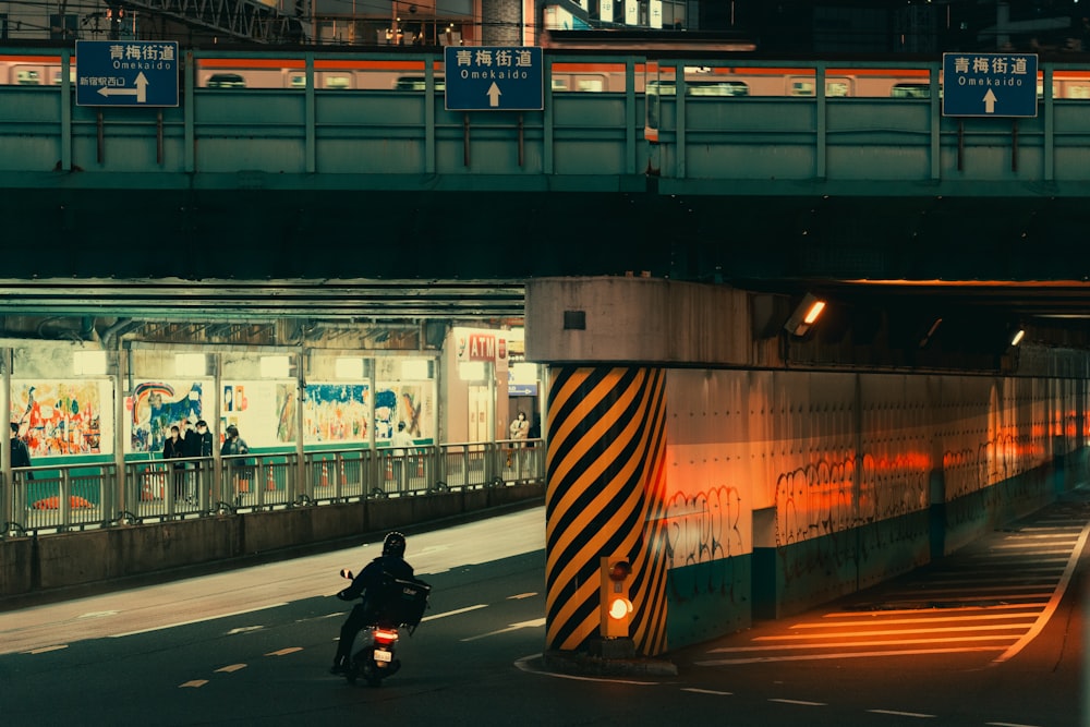 a man riding a motorcycle down a street under a bridge