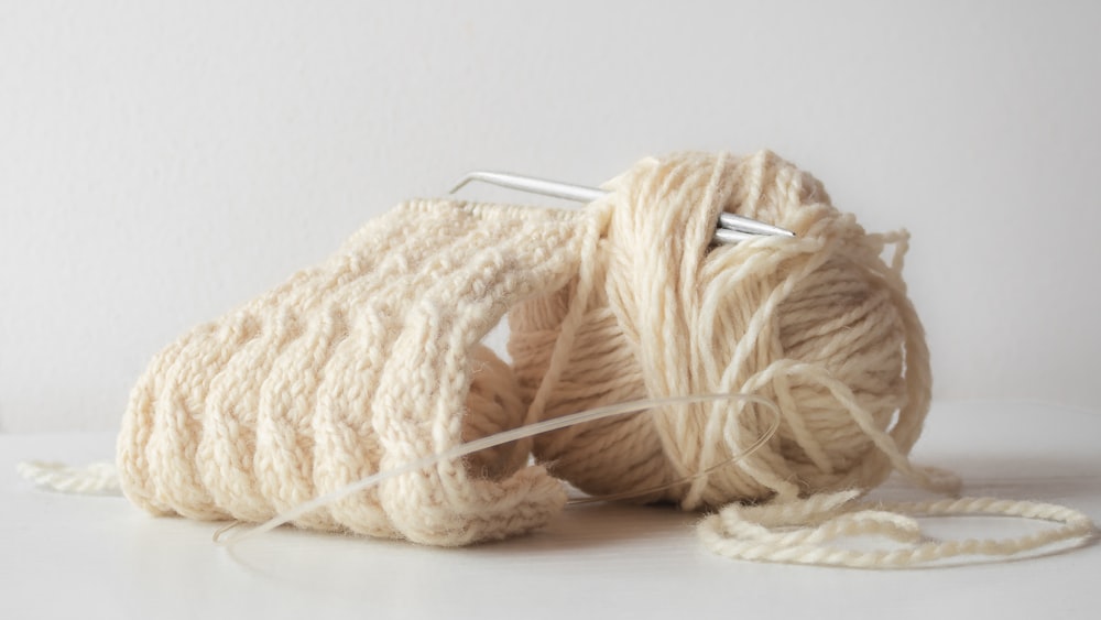 un gomitolo di filo e un ago da maglia su una superficie bianca