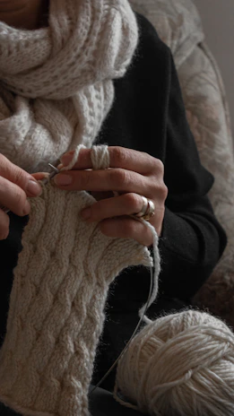 Close-up of hands knitting a wool scarf, soft yarn in deep red hues.
