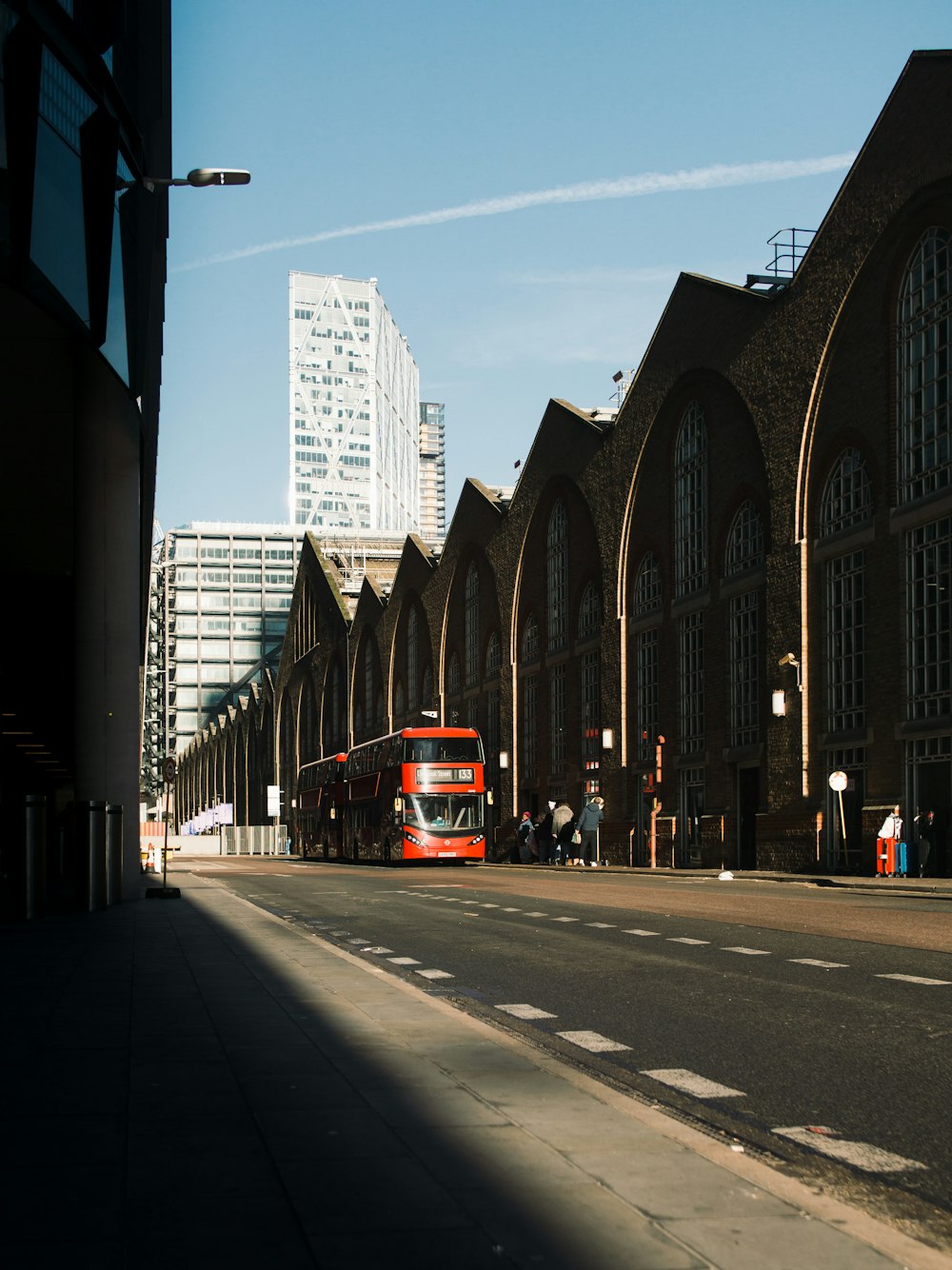 a red double decker bus driving down a street next to tall buildings