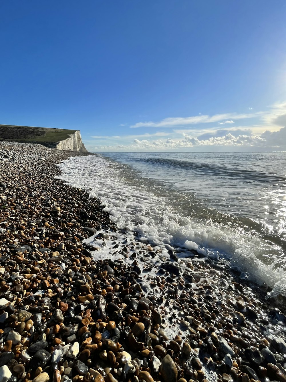 a rocky beach next to the ocean under a blue sky