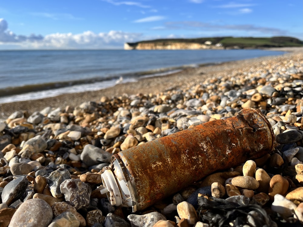 a rusted bottle sitting on top of a rocky beach