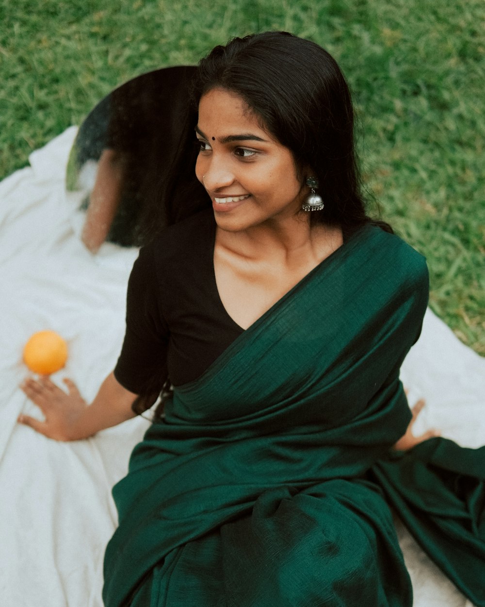 a woman sitting on a blanket holding an orange