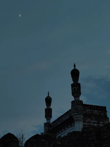 A serene mosque silhouette at sunset with a glowing crescent moon above.