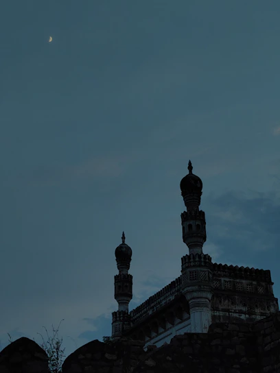 A serene mosque silhouette at sunset with a glowing crescent moon above.