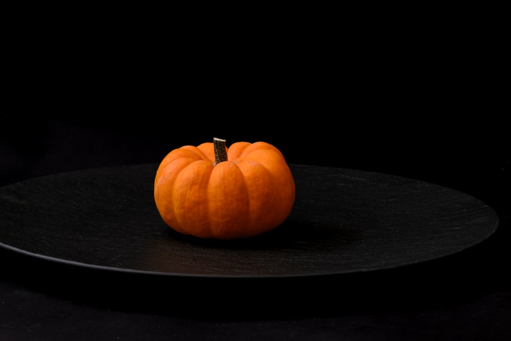 una piccola zucca arancione seduta su un piatto nero