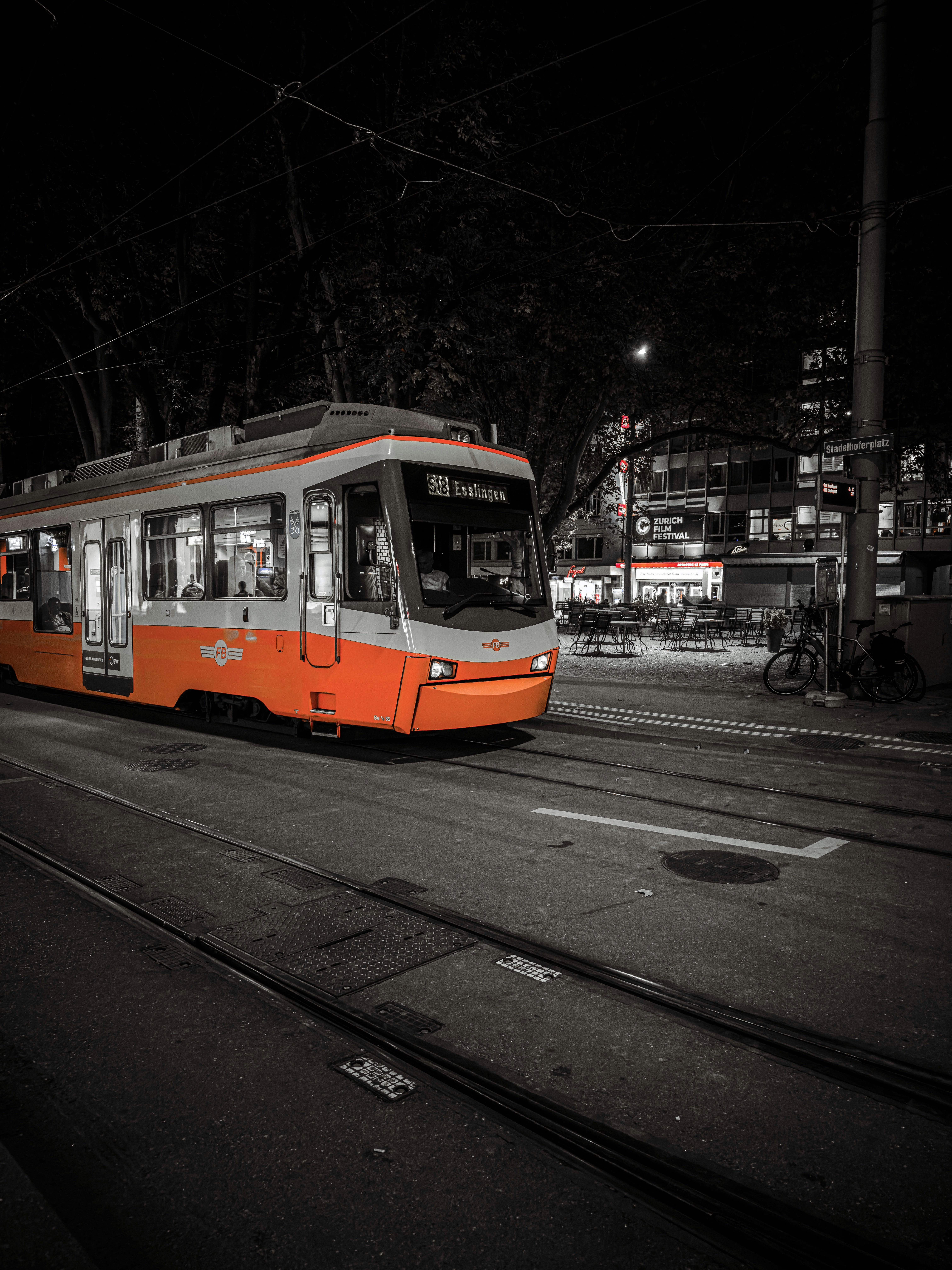an orange and white train traveling down a street at night
