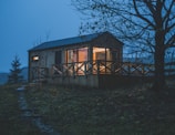 Evening shot of a cabin with warm interior lights glowing through the windows.