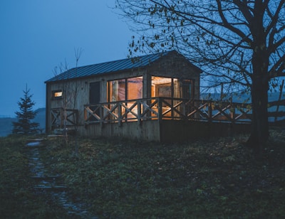 Evening shot of a cabin with warm interior lights glowing through the windows.