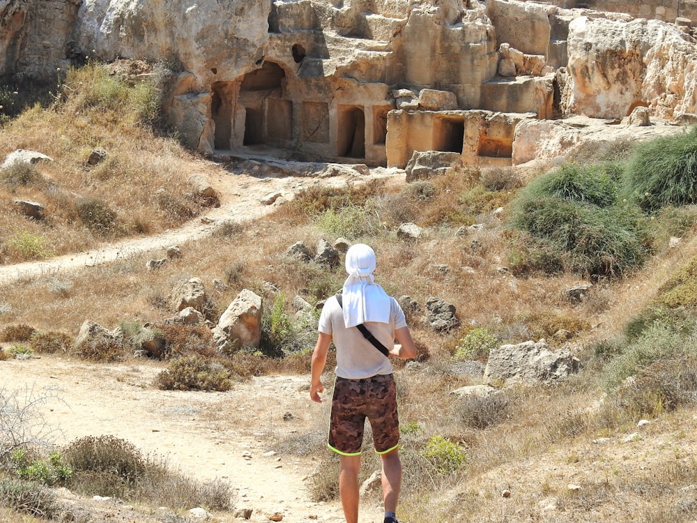 a man walking down a dirt road next to a cliff