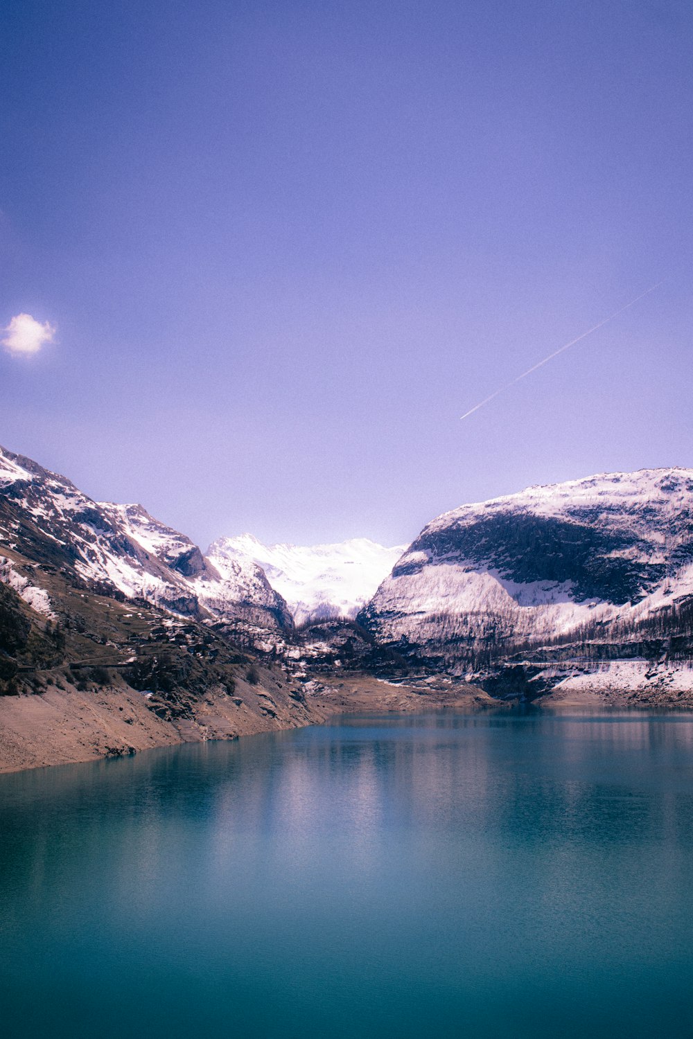 a lake surrounded by snow covered mountains under a blue sky