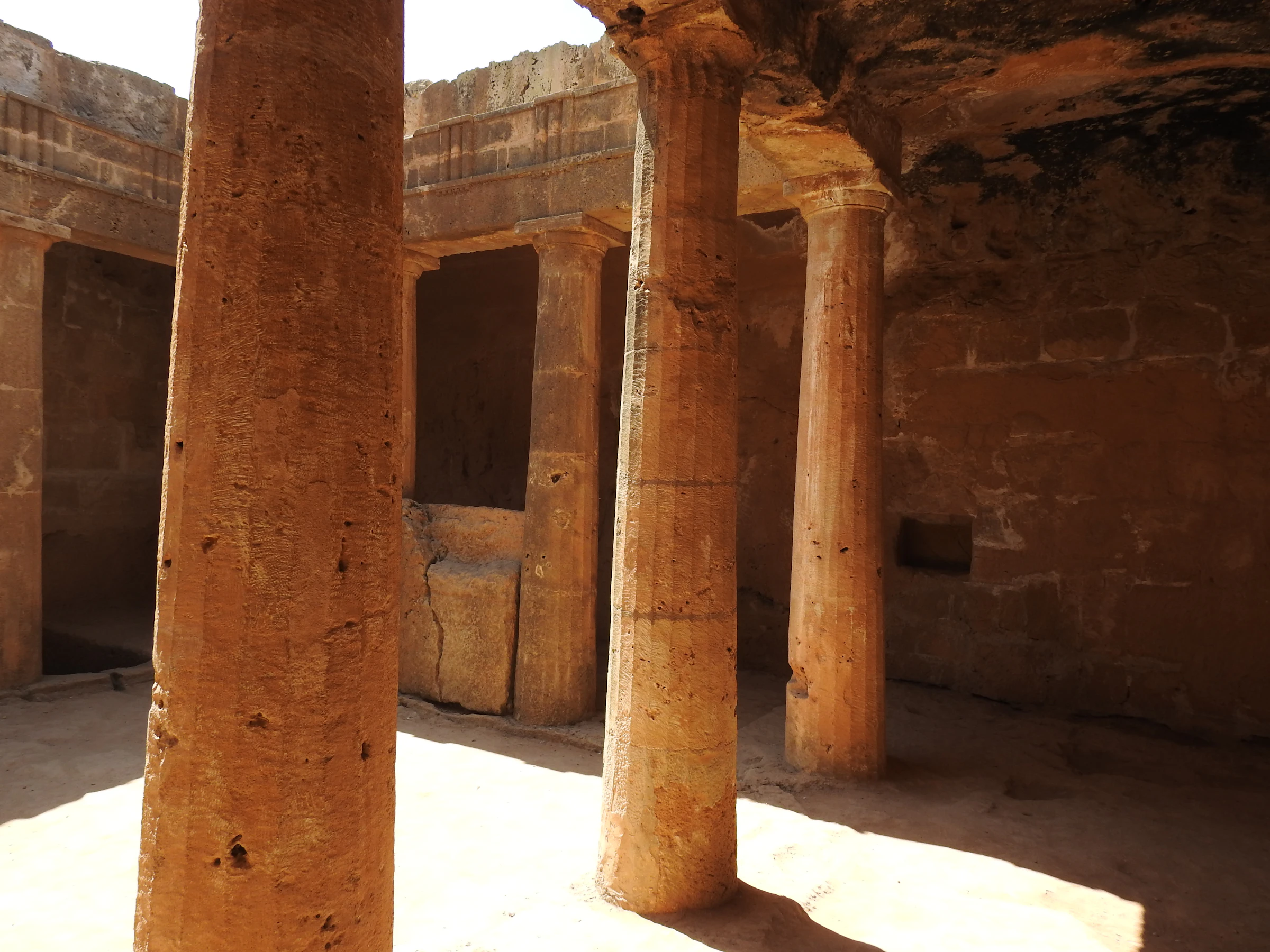 Rock-cut Doric columns around a sunlit underground peristyle courtyard at the Tombs of the Kings in Paphos