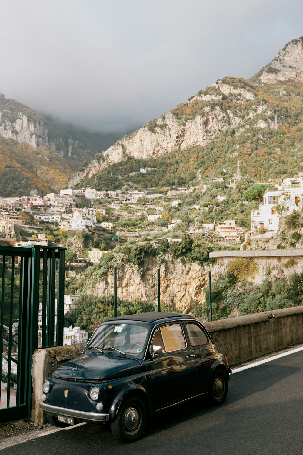 a black car driving down a road next to a lush green hillside