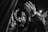A black and white image of a group of people raising their hands in the air, with an expression of unity and possibly celebration or protest. The background is dark, and there is a lamp post illuminating part of the scene.
