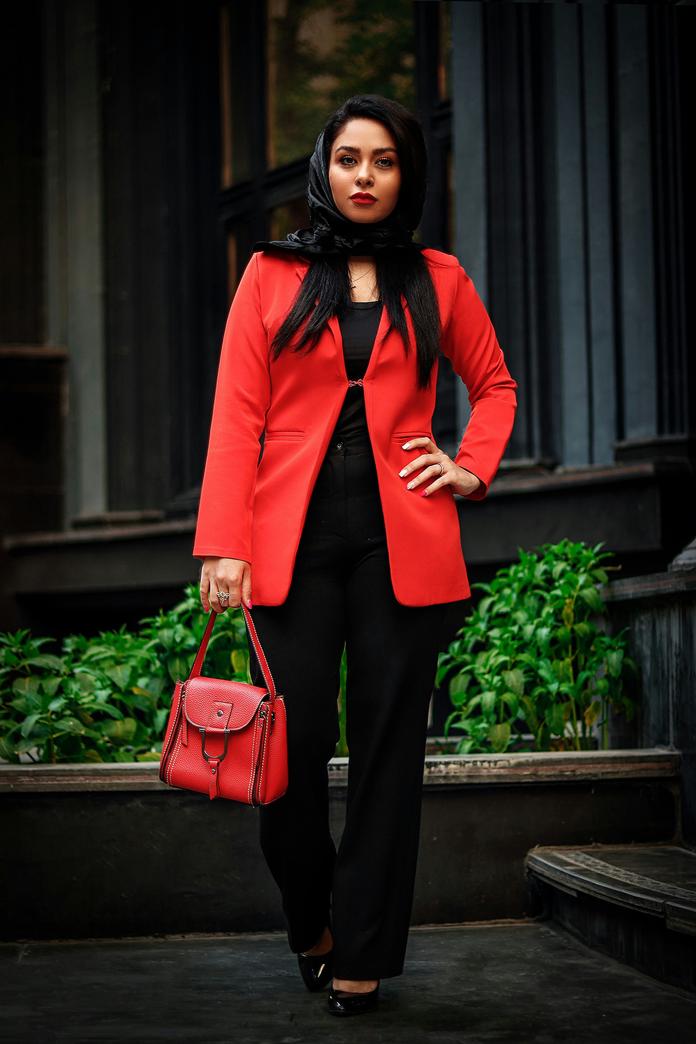 a woman in a red jacket and black pants holding a red purse